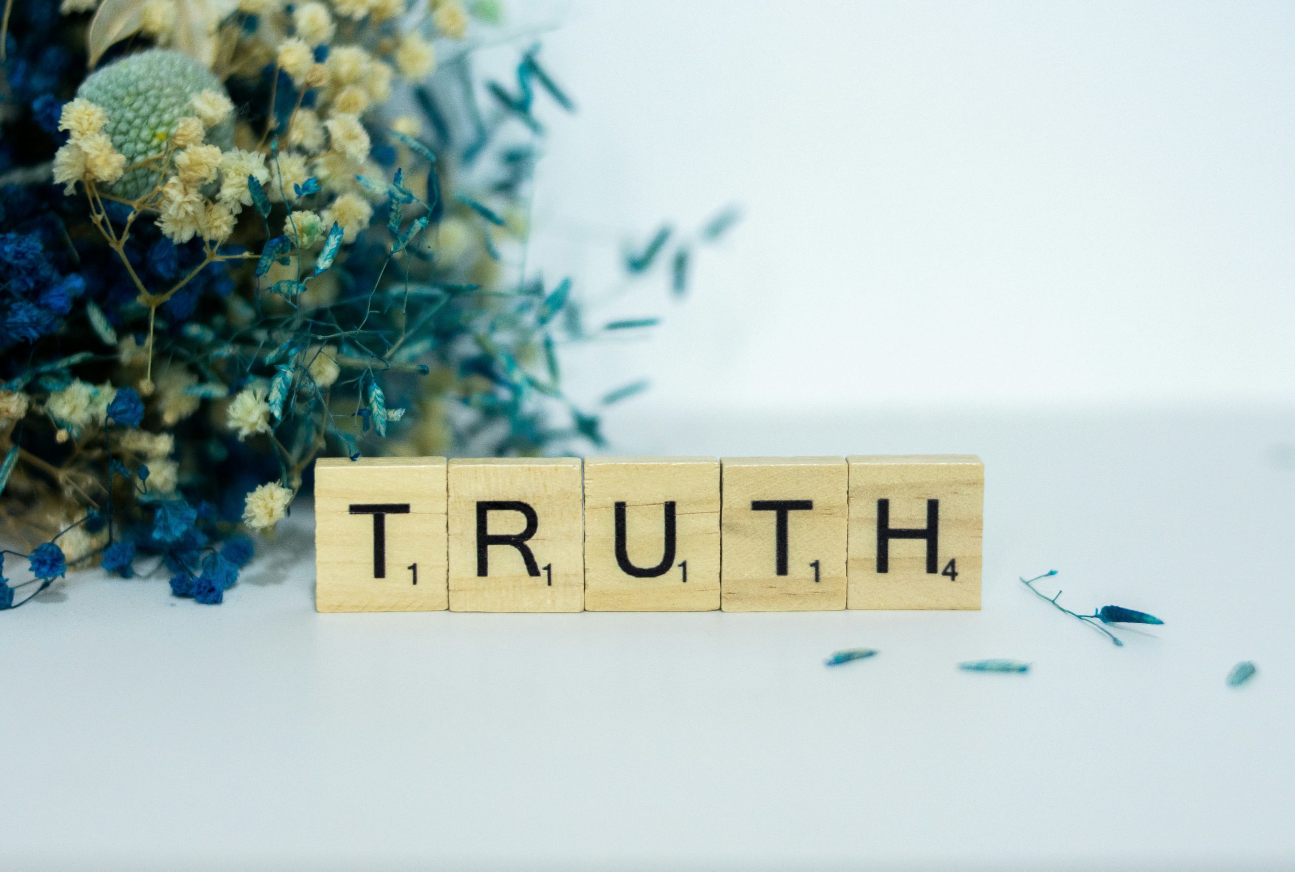 Scrabble tiles writing out the word "Truth" with some plants in the background.